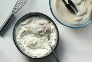 Chicken being coated in the flour mixture.