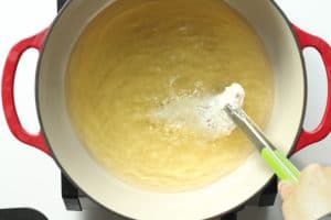 Breaded chicken being dipped in hot frying oil.