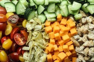 Protein pasta salad with chicken ingredients: cherry tomatoes, artichokes, cheddar cheese, chicken, cucumber.