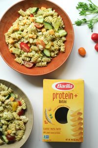Two bowls (orange and beige) of protein pasta salad with chicken and a box of Barilla protein+ pasta.