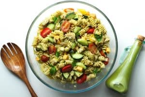 Protein pasta salad in a glass bowl with a bottle of lemon parsley vinaigrette.