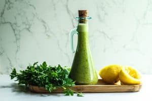 Lemon parsley vinaigrette in a glass bottle with a halved lemon and parsley bunch on the sides.