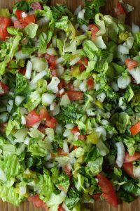 Vegetables for chopped Italian sub sandwiches chopped together on a cutting board.