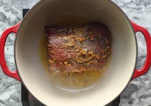 Eye round roast with marinade being seared in oil in a dutch oven.