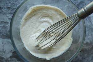 Garlic horseradish aioli being whisked in a clear glass bowl on a gray and white granite surface.
