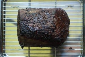 Cooked roast beef resting on a stainless steel baking sheet lined with a wire rack.