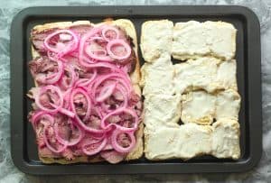 Red onions and sliced roast beef piled on rolls and another side of rolls with garlic horseradish aioli.