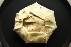 Chicken crunch wrap seam side up on a black plate before being cooked.