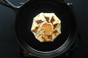 Golden brown chicken crunch wrap seam side up in a cast iron pan.