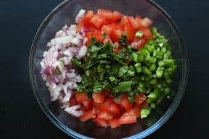 Pico de Gallo ingredients in a clear glass bowl before being mixed on a black surface.