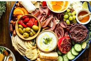 Mediterranean charcuterie board on a blue platter with assorted meats, cheeses, dips, and raw and pickled vegetables