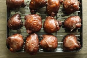Shiny, golden-brown glazed applesauce fritters in lines of four on a baking sheet lined with a cooling rack.