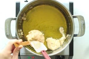 Applesauce fritters batter being dropped into a pot of hot oil to fry.