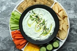 Ranch cottage cheese dip drizzled with olive oil and sprinkled with fresh herbs surrounded by fresh veggies, chips, and crackers.