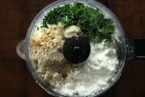 Ranch cottage cheese dip ingredients (fresh herbs and seasonings) in a food processor bowl before being blended.