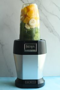 Green protein smoothie ingredients like spinach, mango, and banana in a blender.
