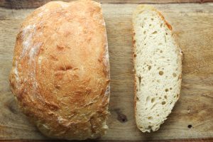 A loaf of sourdough bread with a slice cut next to it on a wooden cutting board.