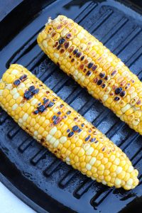Corn cobs being charred on a cast iron grill pan.
