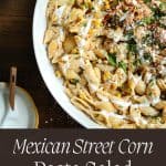 Mexican street corn pasta salad text overlay with the pasta salad in a white bowl with lime wedges.