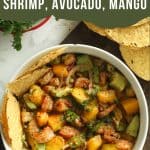 Shrimp, avocado, and mango salad in a bowl on a cutting board with tostadas.