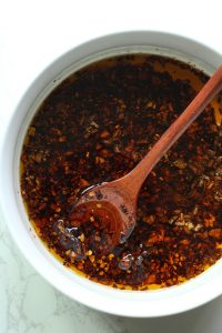 A white bowl filled with homemade chili crisp with a wooden spoon.