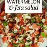 A bowl of watermelon salad with feta cheese sprinkled with chili crisp and fresh mint and basil.