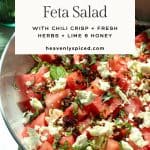 A bowl of watermelon salad with feta cheese with recipe title text overlay mentioning chili crisp, fresh herbs, lime + honey.