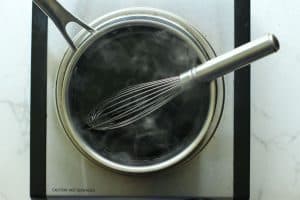Balsamic glaze in a stainless-steel pot with steam coming out and a wire whisk.