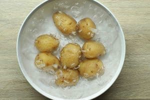 Potatoes in an ice bath in a white bowl on light-colored wooden surface.