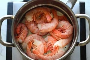 Large pink uncooked shrimp in the shells in a steamer basket.