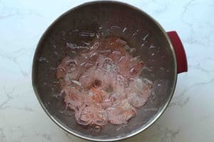 Cooked shrimp in an AVACRAFT bowl filled with ice and water on a white and grey granite surface.