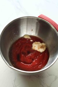 A stainless steel bowl filled with cocktail sauce ingredients: ketchup, Worcestershire, lemon juice, and horseradish.