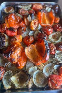 Roasted tomatoes, onions, red bell peppers, and garlic on a sheet tray for roasted tomato basil and red pepper soup.