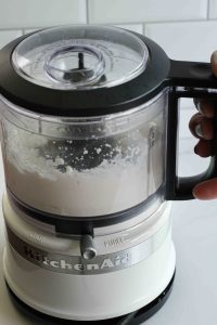 Cottage cheese being blended in a white KitchenAid brand food processor bowl.