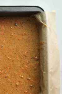 A close up of carrot cake loaf cake batter in a parchment lined loaf pan.