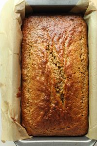 A fully baked and golden carrot cake loaf cake in a parchment lined loaf pan.