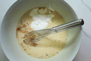 Cottage cheese and vanilla extract added to carrot cake loaf cake batter in a white bowl with a silver stainless steel whisk.