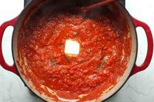 A pad of butter in the middle of a pot of marinara sauce before being stirred.