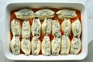 Uncooked beef stuffed shells lined in a baking dish.
