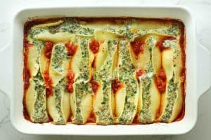 Cooked beef stuffed shells over marinara sauce lined in a white baking dish on a white granite surface.