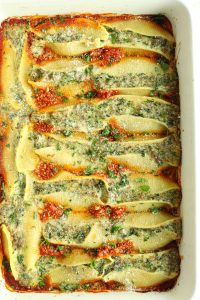 Beef stuffed shells lined over marinara sauce topped with grated parm and chopped parsley in a white baking dish.