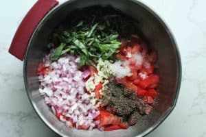 Bruschetta ingredients: tomato, red onion, garlic, basil, salt, and pepper, before being mixed, in a silver bowl.