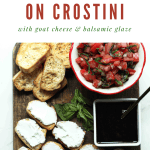 Bruschetta on crostini with goat cheese & balsamic glaze on a wooden board.