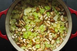 A dutch oven filled with tom yum noodle soup ingredients after the cabbage and mushrooms were added.