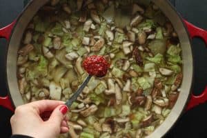 A pot of tom yum noodle soup with a spoonful of chili garlic sauce being held overtop before adding in.