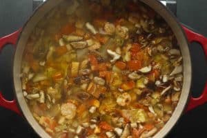 A dutch oven with red handles with tom yum soup filled with shrimp, mushrooms, tomatoes, cabbage, onions, etc.