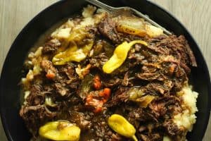 Instant pot mississippi pot roast over mashed potatoes in a black bowl and topped with whole pepperoncinis.