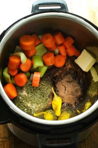 Mississippi pot roast ingredients in the instant pot: au ju gravy mix, homemade ranch seasoning, pepperoncinis, carrots, celery, onion, chuck roast, butter.