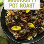 Easy and delicious Mississippi pot roast over mashed potatoes and topped with whole peperoncini peppers in a black bowl.